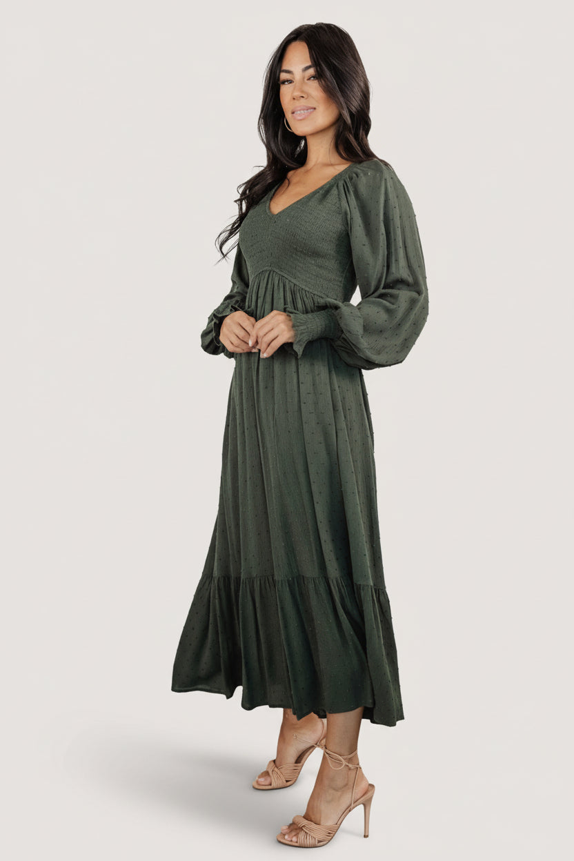Side profile of the deep olive midi dress showing smocked bodice, elastic shoulder detail, and tiered hem on a model.