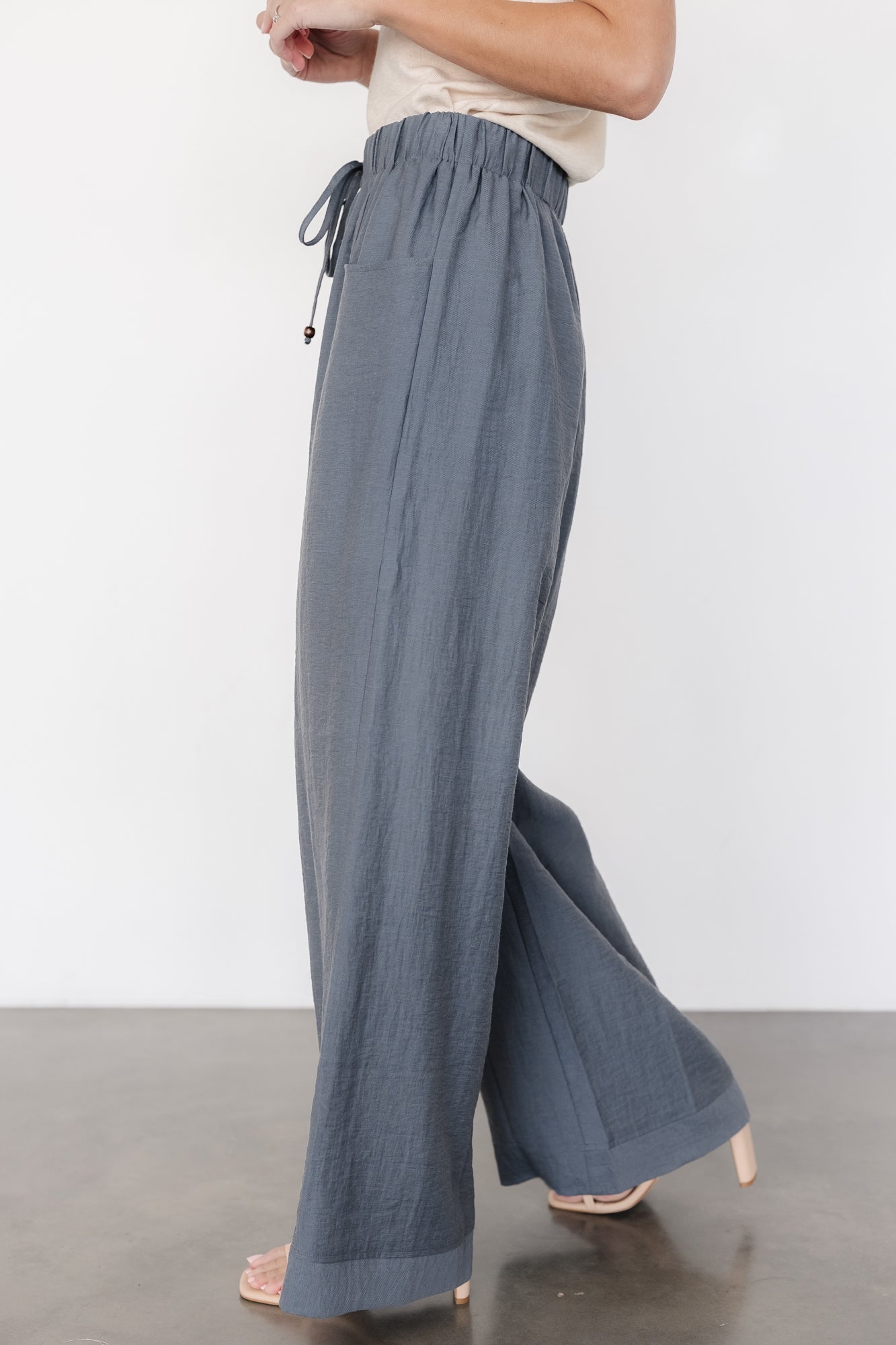 Back and side view of slate blue wide-leg pants displaying pocket placement, stitched hem, and relaxed silhouette suitable for everyday wear.