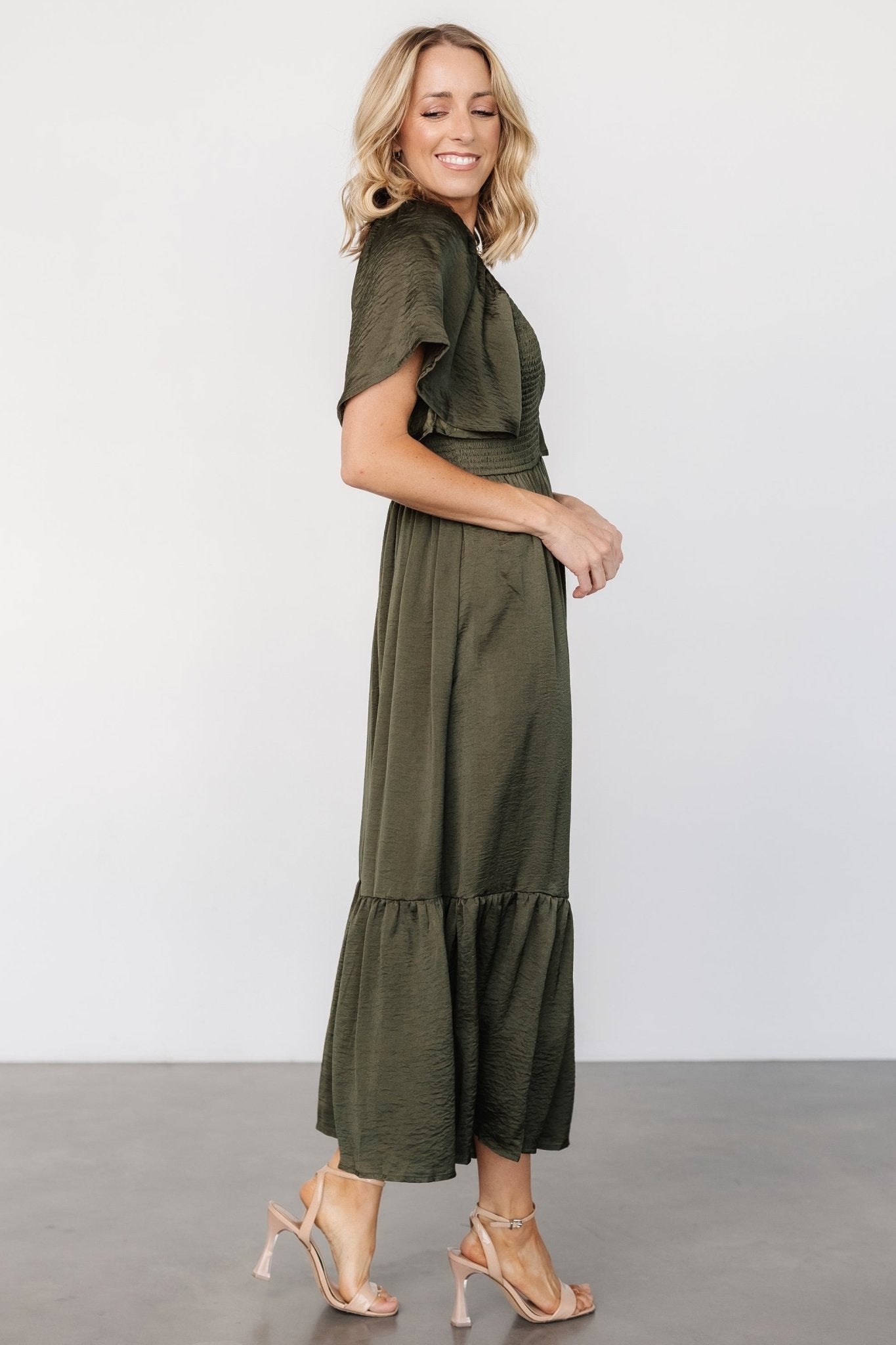 Detail image of Lovell smocked midi dress hem showing semi-pleated ruffle edge and soft satin-like drape in deep olive.