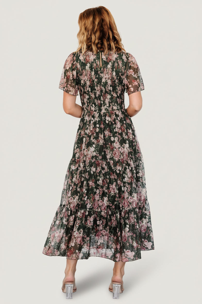 Model wearing dark green embroidered tulle midi dress, showing overall fit, smocked bodice, ankle-length tiers, and floral details.