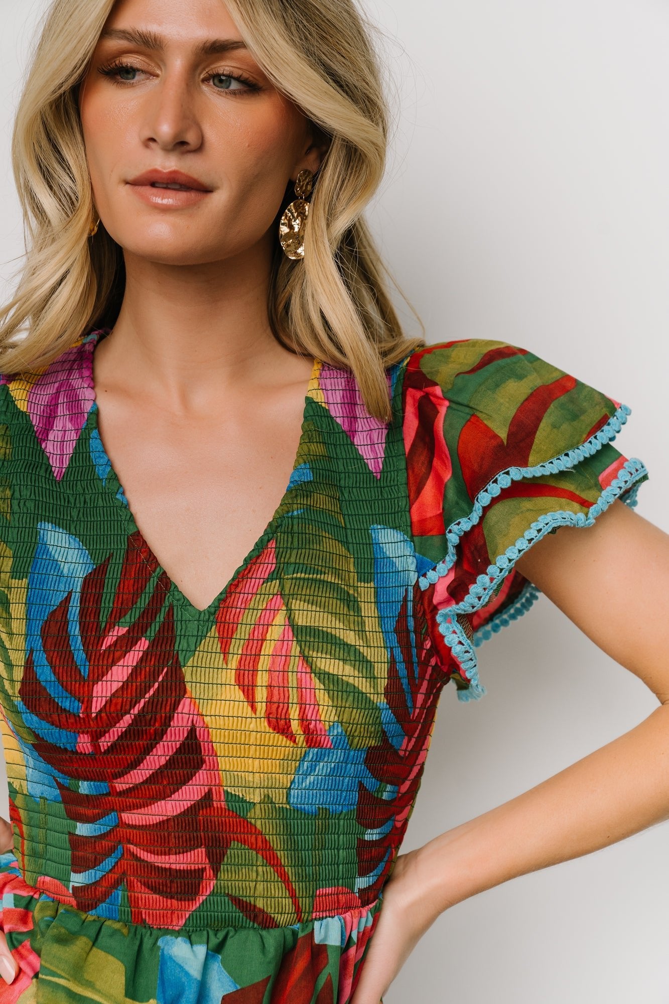 Model wearing Marielle smocked midi dress in multicolor leaf print; side view shows hidden pockets and elastic waistband.