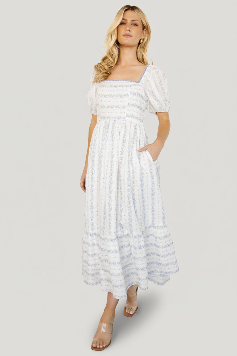 Styling image of Martine Puff Sleeve Midi Dress in ivory multi floral with visible hidden side pocket and soft tiered skirt movement.