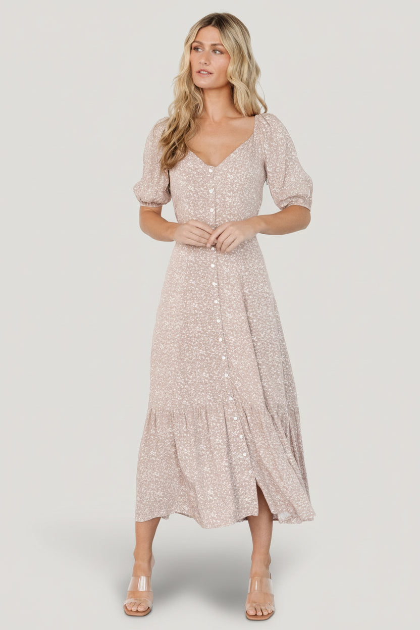 Lifestyle shot of a model wearing a beige floral maxi dress with puff sleeves and tiered skirt, styled casually with sandals for daytime wear.