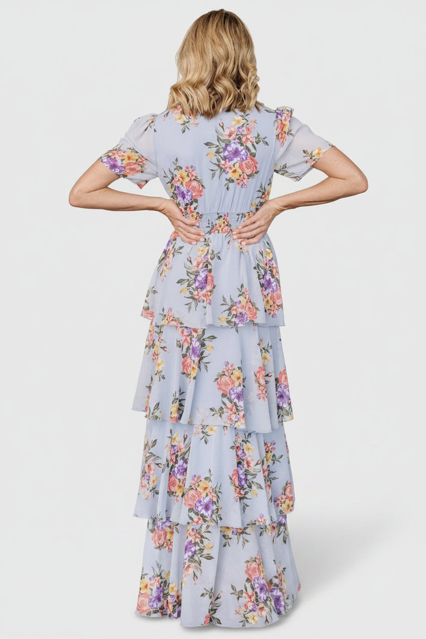 Model walking in light blue floral ruffle maxi dress, showing full skirt sweep, short sleeves, and event-ready styling possibilities.