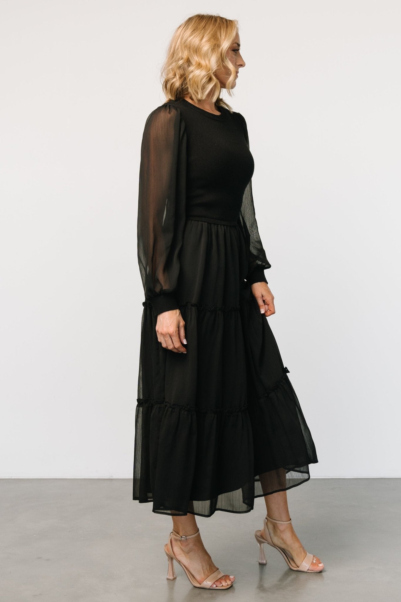 Studio shot of Remi ribbed maxi dress in black laid flat showing tiered skirt silhouette and sweater-knit bodice texture.