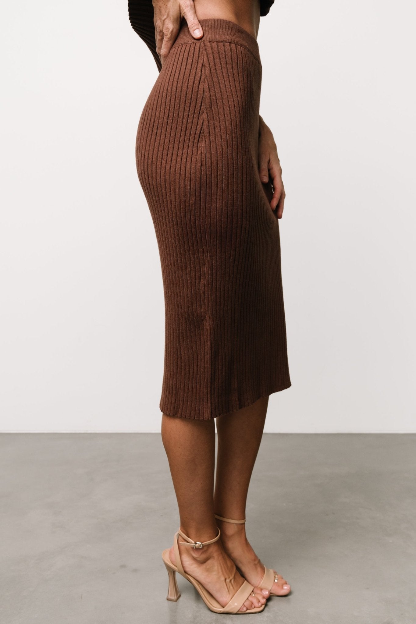 Studio flat-lay of brown ribbed midi skirt showing fabric texture, rib pattern, waistband detail, and overall knit construction.