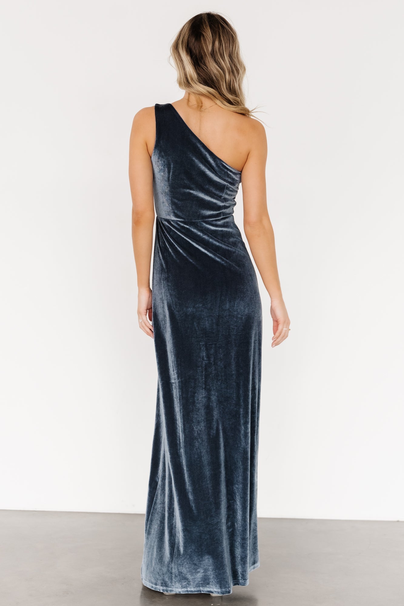 Model wearing Tatiana velvet one-shoulder maxi in slate blue, fitted through the bodice with a slight flare at the hem.