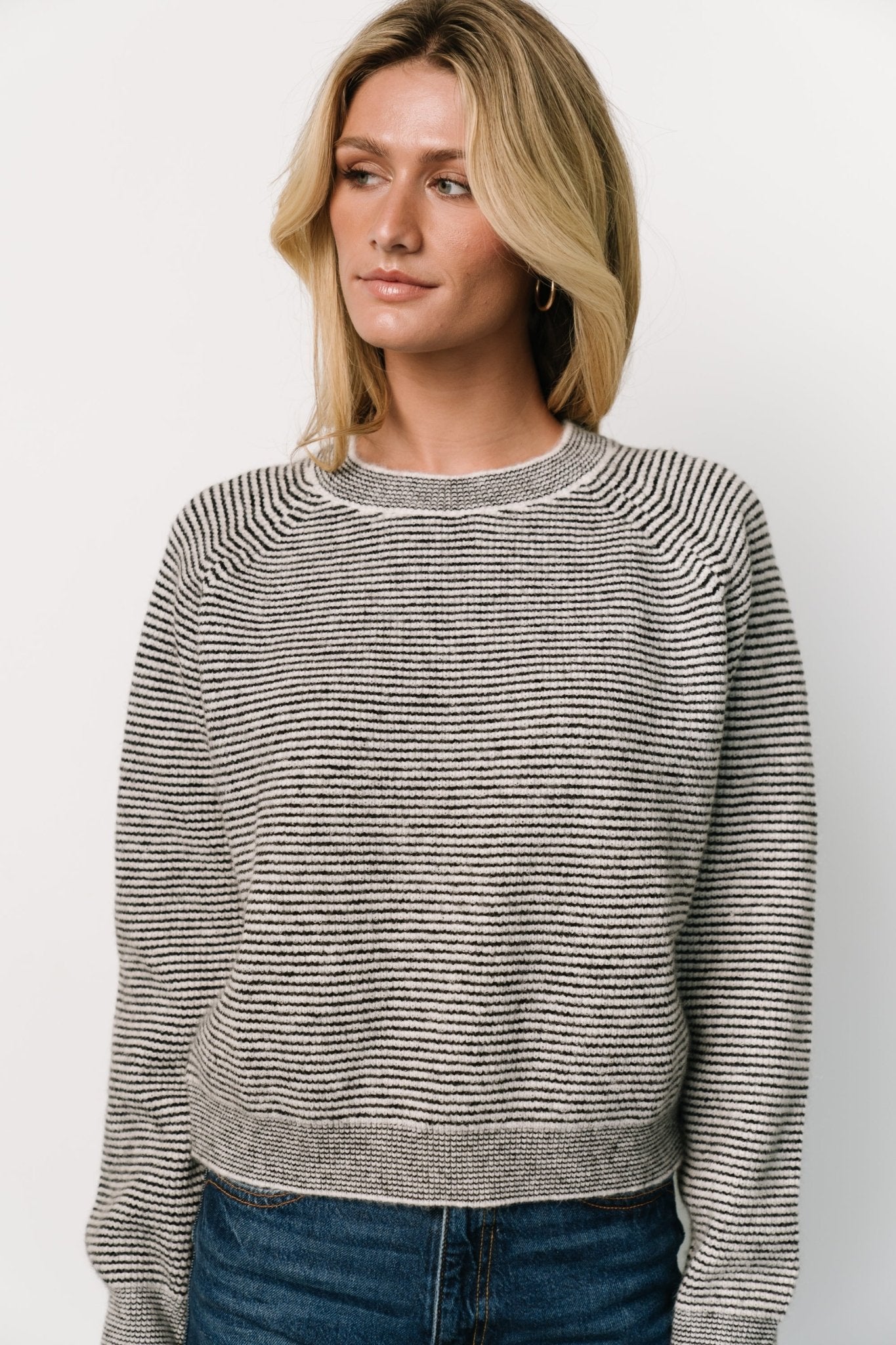 Model wearing the Zadie Striped Sweater in ivory and black styled with casual jeans to demonstrate length and everyday wearability.