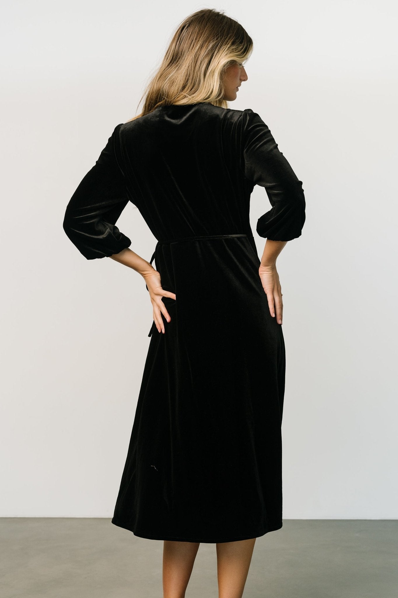 Lifestyle angle of the wrap midi in black velvet showing movement in the skirt and the flattering wrap closure at the waist.