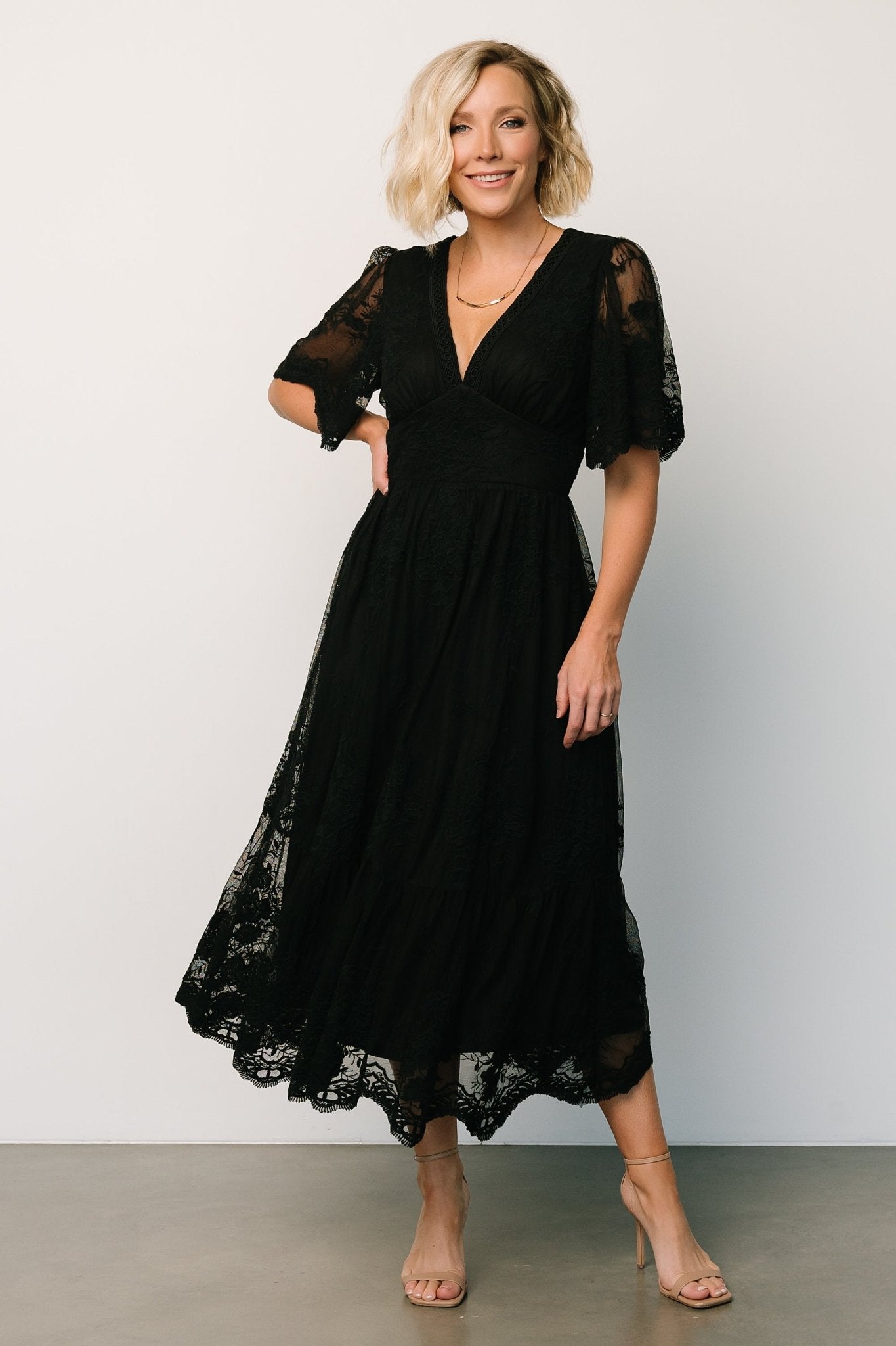 Detail image of embroidered lace and scalloped hem on a black midi dress showing texture, lining contrast, and delicate sleeve sheerness for close inspection.