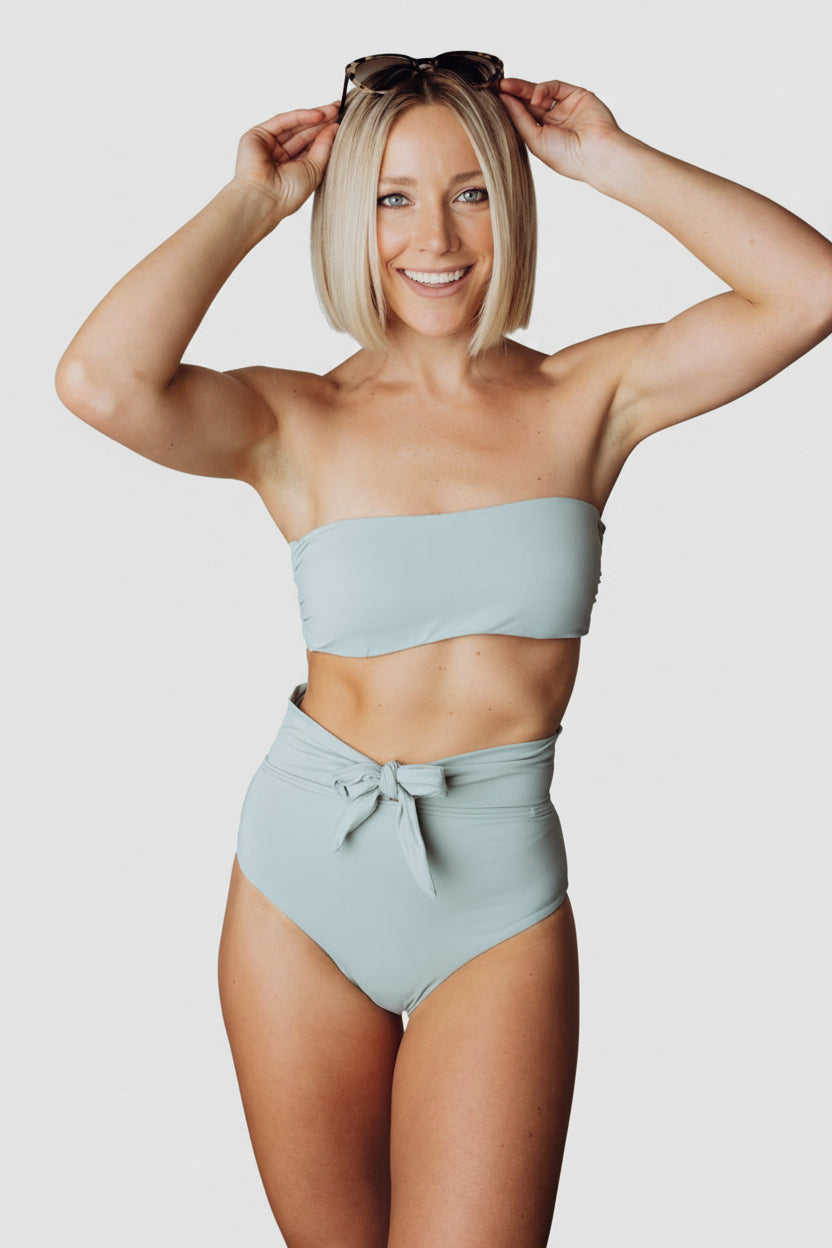 Front view of Milos sage bandeau bikini top on model showing tie-back detail, removable pads, and smooth nylon-spandex fabric in sage tone.
