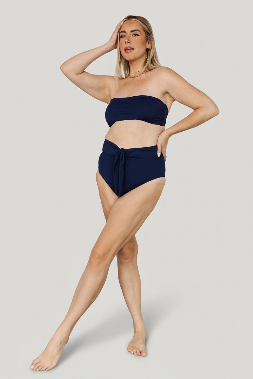 Side view of navy high-waist bikini bottom highlighting adjustable front wrap tie, fabric stretch, and mid-rise profile for comfortable wear.