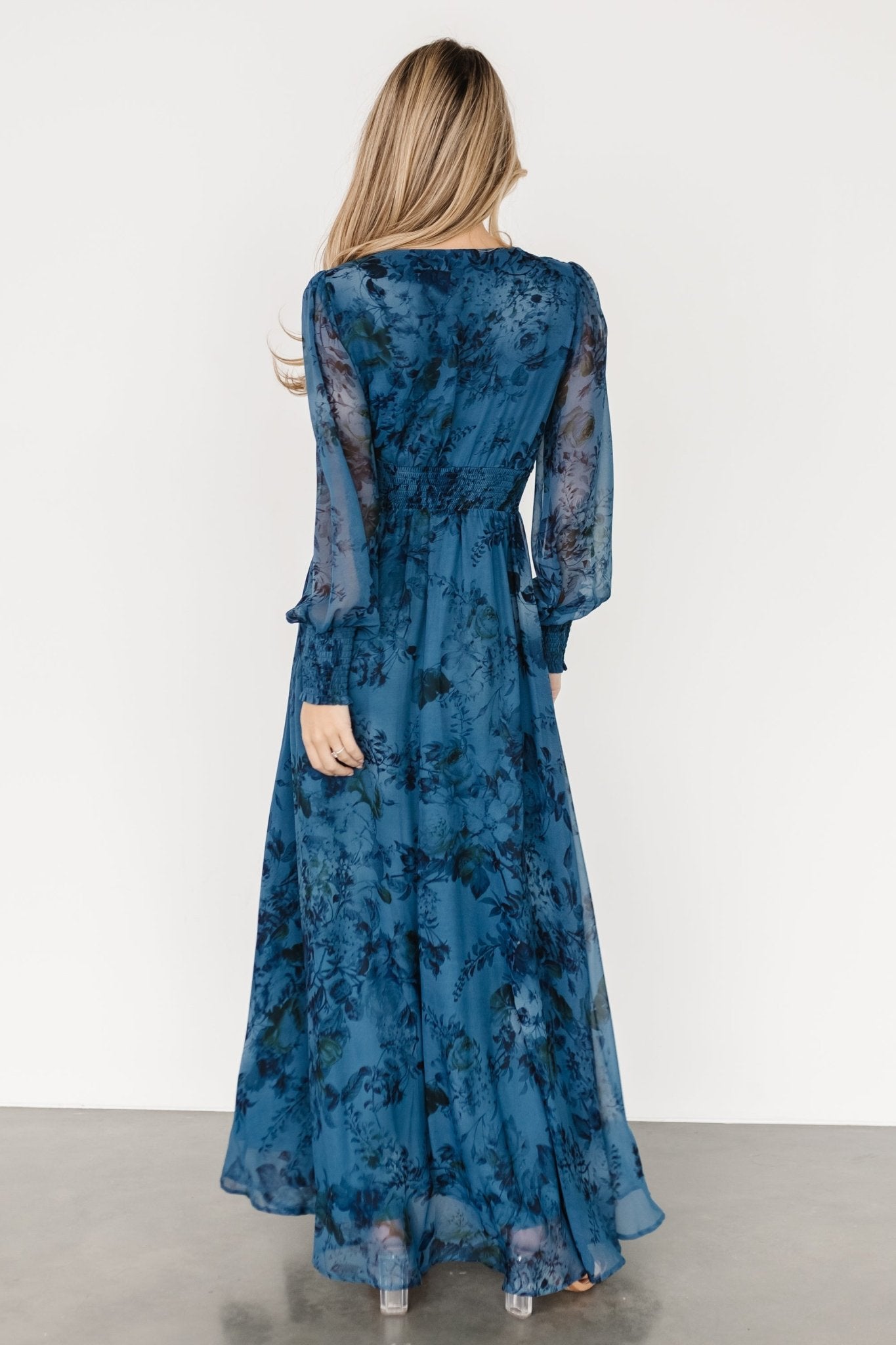 Side profile of model in deep blue floral maxi showing long sleeve movement and full skirt drape.