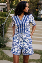 Front view of blue and ivory floral Rafaela Romper featuring V-neck, embroidered bodice panels, short oversized sleeves, and shorts with pockets.