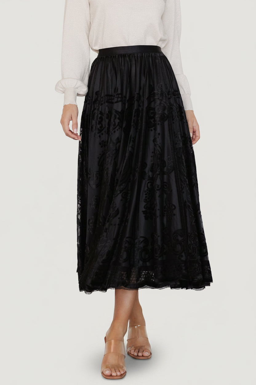 Front view of a model wearing the Palini Velvet Burnout Midi Skirt in black, showing the skirting silhouette and elastic waistband, mid-length.