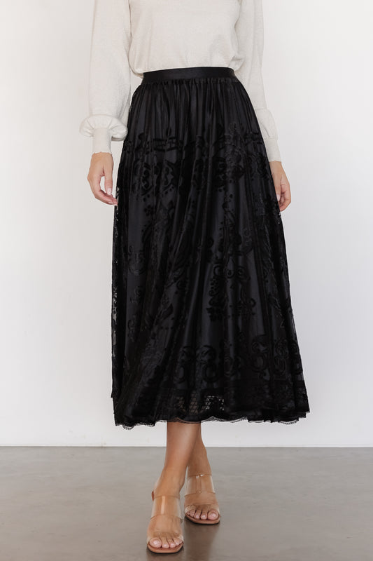 Front view of a model wearing the Palini Velvet Burnout Midi Skirt in black, showing the skirting silhouette and elastic waistband, mid-length.
