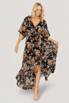 Three-quarter view showing crossover surplice neckline and loose kimono sleeves on the Kia Kimono Maxi Dress in Black + Copper Floral.