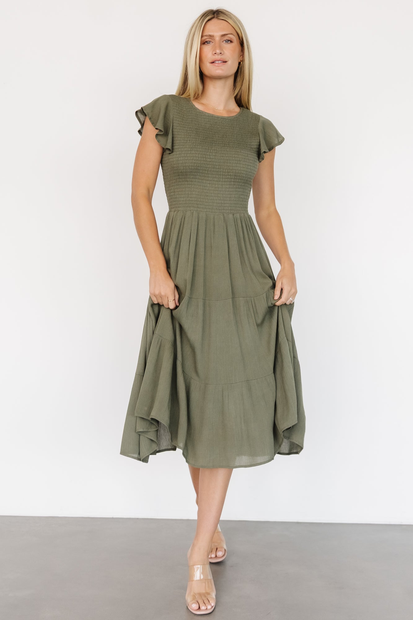 Front view of Loretta Smocked Midi Dress in dark sage showing smocked bodice, round neckline, flutter sleeves, and three-tiered midi skirt.