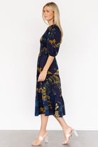 Full-length shot of the Lena Tiered Midi Dress in navy with gold floral pattern, showing silhouette, midi length and tiered movement on model.