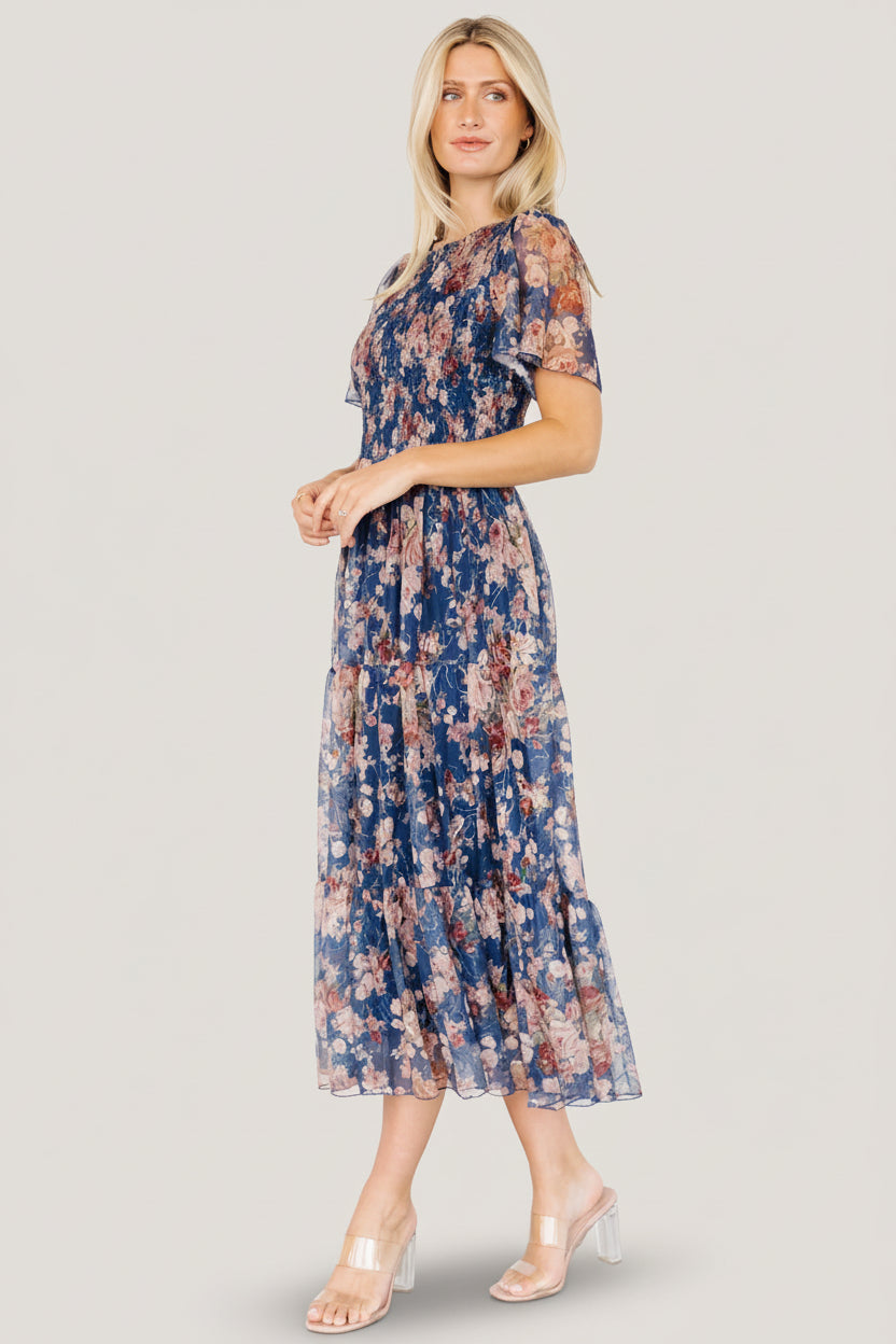 Close-up of embroidered florals on dark blue tulle with delicate gold-thread detailing and textured stitching visible on the overlay fabric.