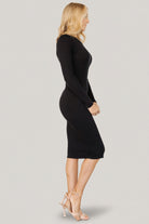 Side profile of the Mavis ribbed midi dress in black on model, showing midi length skirt, long sleeve fit, and raw hem detail.
