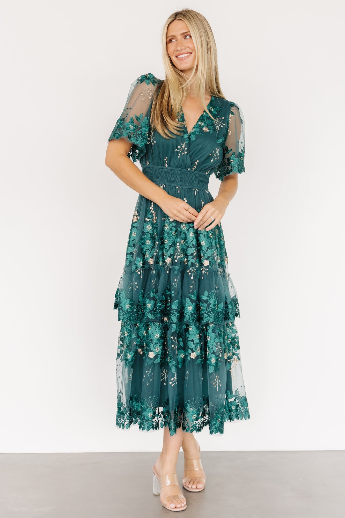 Model wearing Lotte dress in emerald, full-length view highlighting midi hem, tiered ruffle overlay and soft tulle movement as she poses.