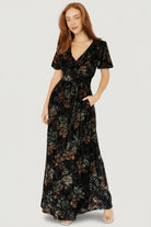 Three-quarter view showing embossed velvet floral texture and gathered waist detail on the Leslie Velvet Maxi Dress; side pockets visible.
