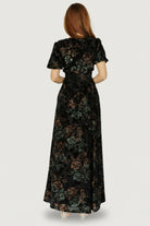 Back view of Leslie Velvet Maxi Dress in Black and Deep Jade Floral, showing full lining, skirt length, and back silhouette.