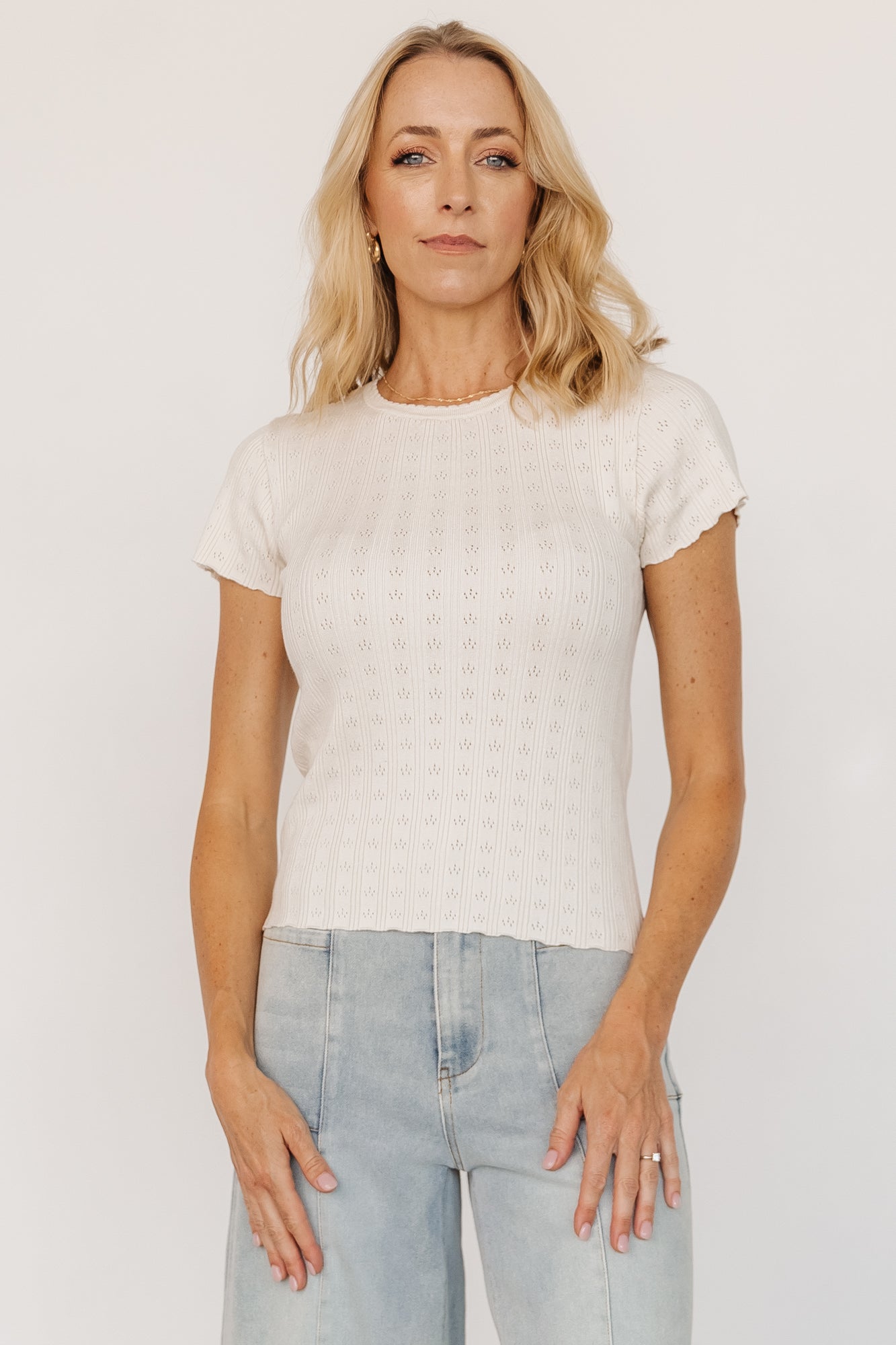 Three-quarter view of model wearing the ivory Penny Pointelle Top, highlighting ribbed detailing and scalloped sleeve cuffs.