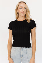Side view of Penny Pointelle knit top in black showing short sleeve length, curved scalloped hem, and soft drape of the viscose-blend fabric.