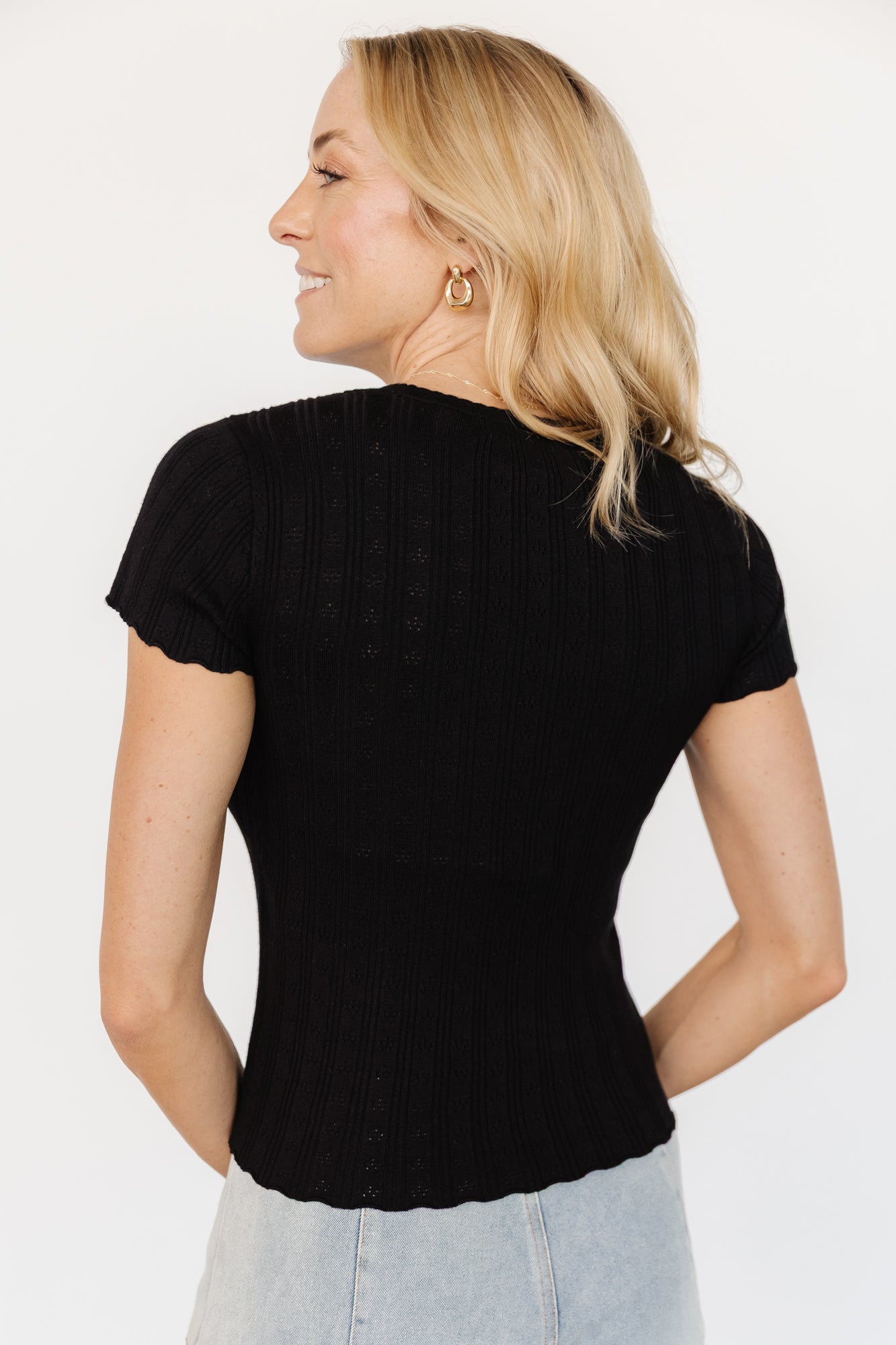 Back view of Penny Pointelle Top in black on model, displaying ribbed texture across the back and scalloped edge at the hem for feminine detail.