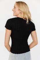 Back view of Penny Pointelle Top in black on model, displaying ribbed texture across the back and scalloped edge at the hem for feminine detail.