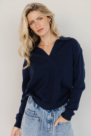 Front view of navy Bodhi sweater on model showing open rugby collar, dropped shoulders, ribbed cuffs, and relaxed drape across the torso.