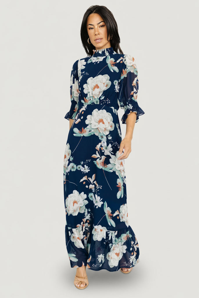 Front view of navy floral chiffon maxi dress on model showing smocked high neck, short ruffle sleeves, and flowing single-tiered skirt.