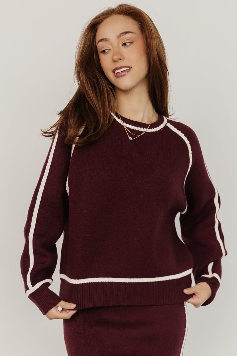 Model wearing Ava knit sweater in deep wine, front view showing round neckline and cream piping, relaxed tailored fit and soft drape.