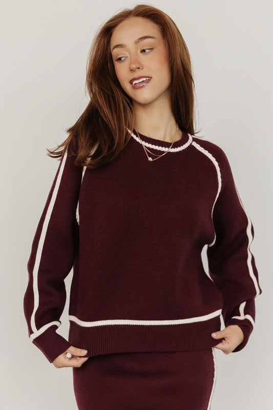 Model wearing Ava knit sweater in deep wine, front view showing round neckline and cream piping, relaxed tailored fit and soft drape.