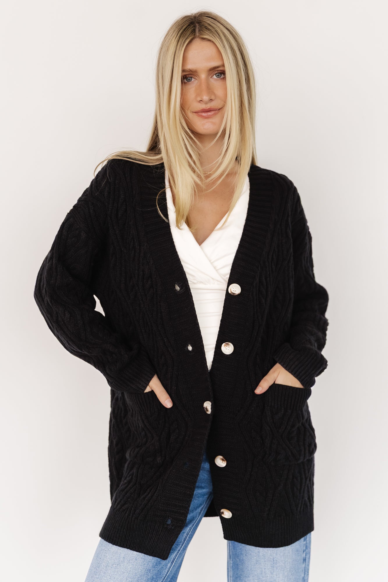 Front view of Alberta cable knit cardigan in black on model, showing chunky cable texture, dropped shoulders, wide ribbed placket, and five-button closure.