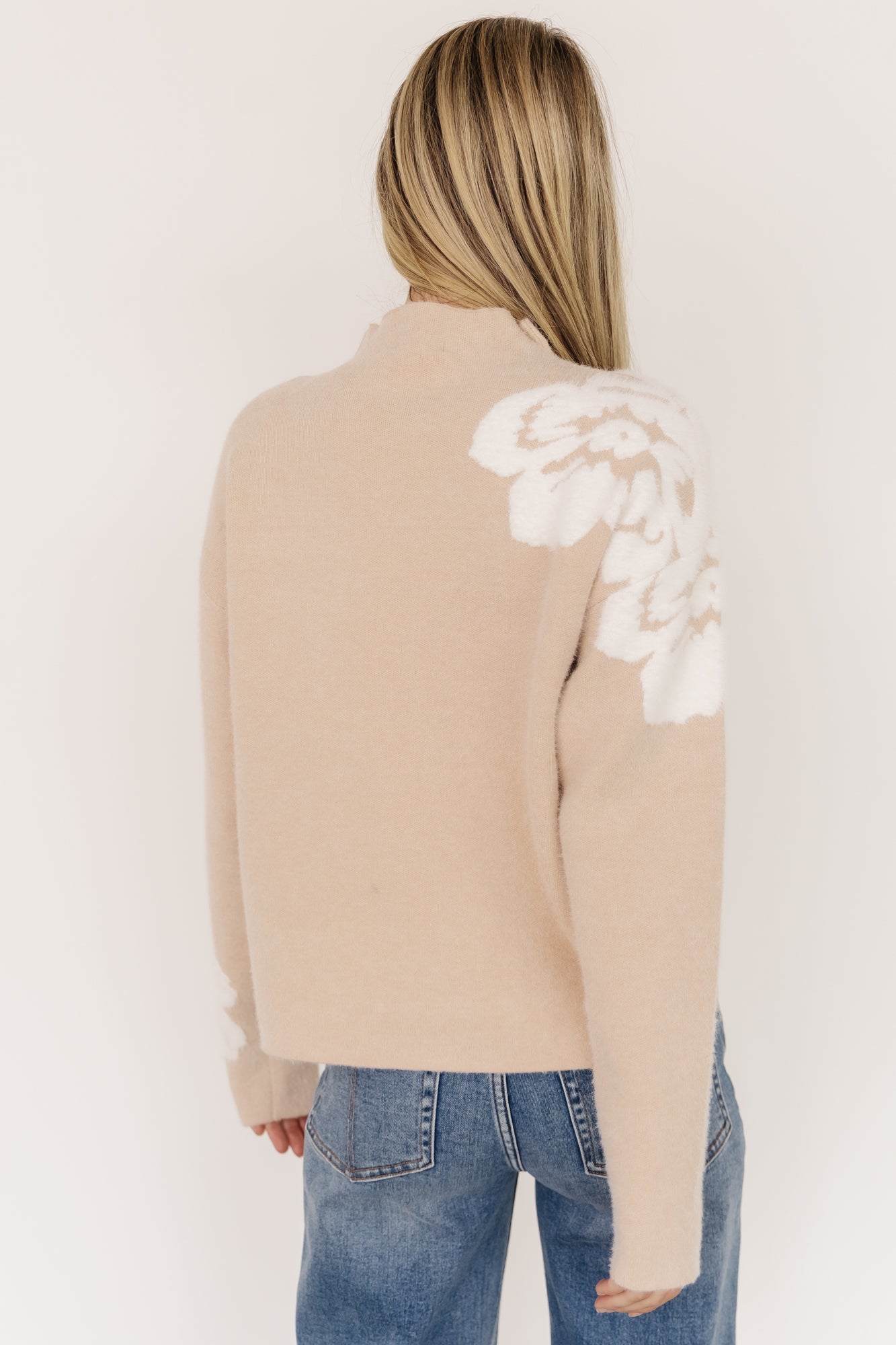 Detail of left sleeve cuff with embroidered accent flower and close-up of the wide knit texture at the hem and cuff.
