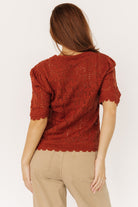 Styled flat-lay of Serenity Knit Sweater Top in rust paired with high-waist denim to show cropped length and scalloped hem detail.