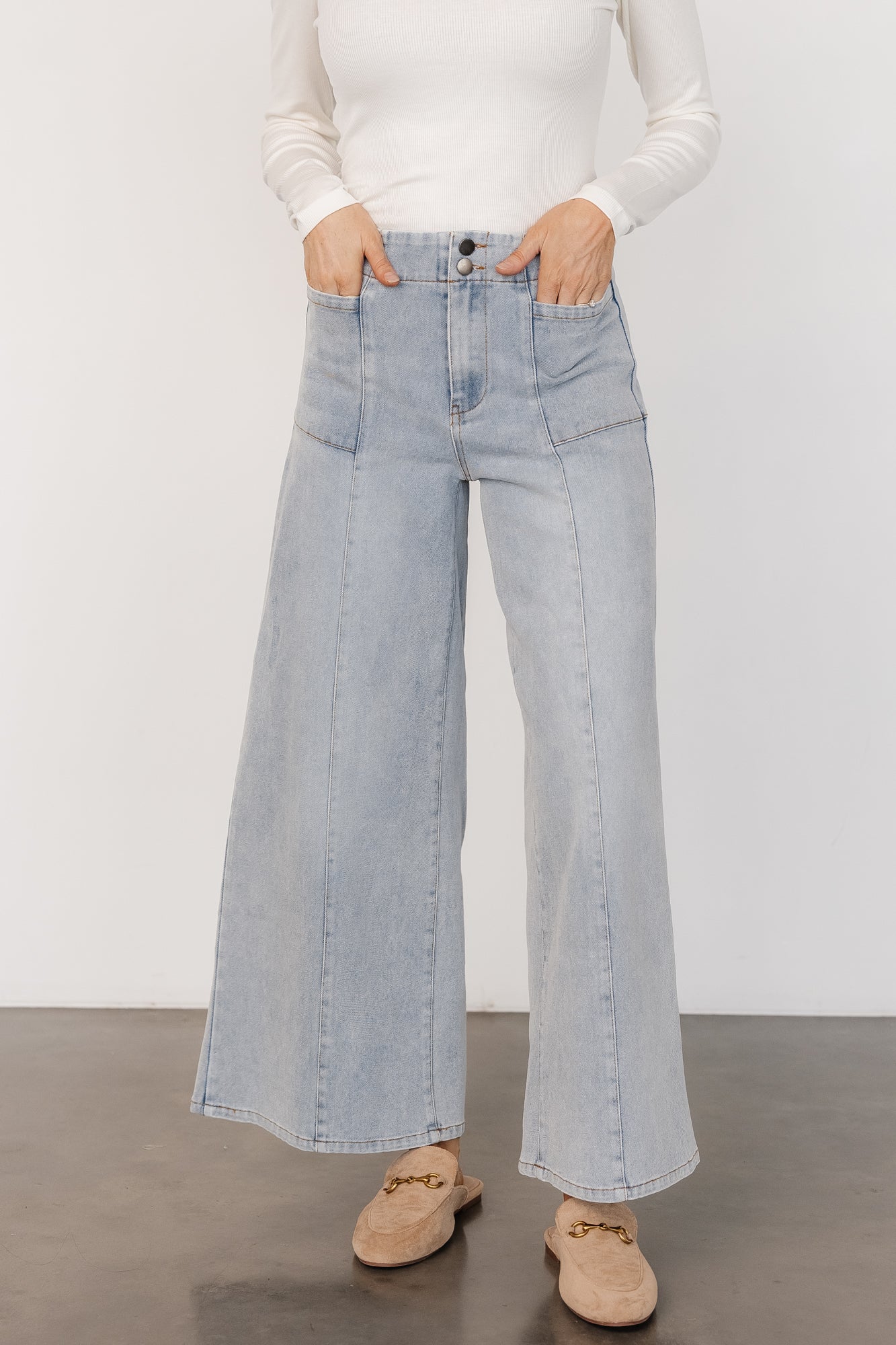 Front view of Emmi mid-rise wide-leg jeans in light wash worn by model, showing full-length flare and visible front pockets for styling.