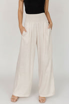Front view of model wearing Parvati smocked high-waist wide-leg pants in natural linen-rayon blend, showing smocked waist and side pockets.
