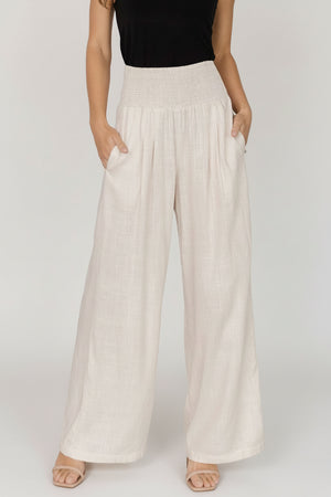 Front view of model wearing Parvati smocked high-waist wide-leg pants in natural linen-rayon blend, showing smocked waist and side pockets.