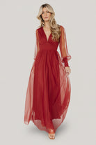 Three-quarter side view of Layla Tulle Maxi Dress in terracotta showing flowing tulle skirt, smocked cuffs, and the raw hemline; model poses mid-step.