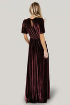 Styled full-length shot of the Vivian Velvet Maxi Dress in Clove on a model, showing flutter sleeves, sweeping skirt, and the dress’s rich, brown-purple hue.