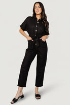 Front view of model wearing the Dallas black linen button-up jumpsuit with cuffed short sleeves, self-tie sash and tapered cropped pant legs.