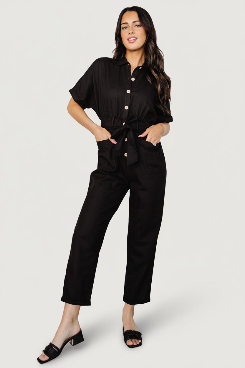 Front view of model wearing the Dallas black linen button-up jumpsuit with cuffed short sleeves, self-tie sash and tapered cropped pant legs.