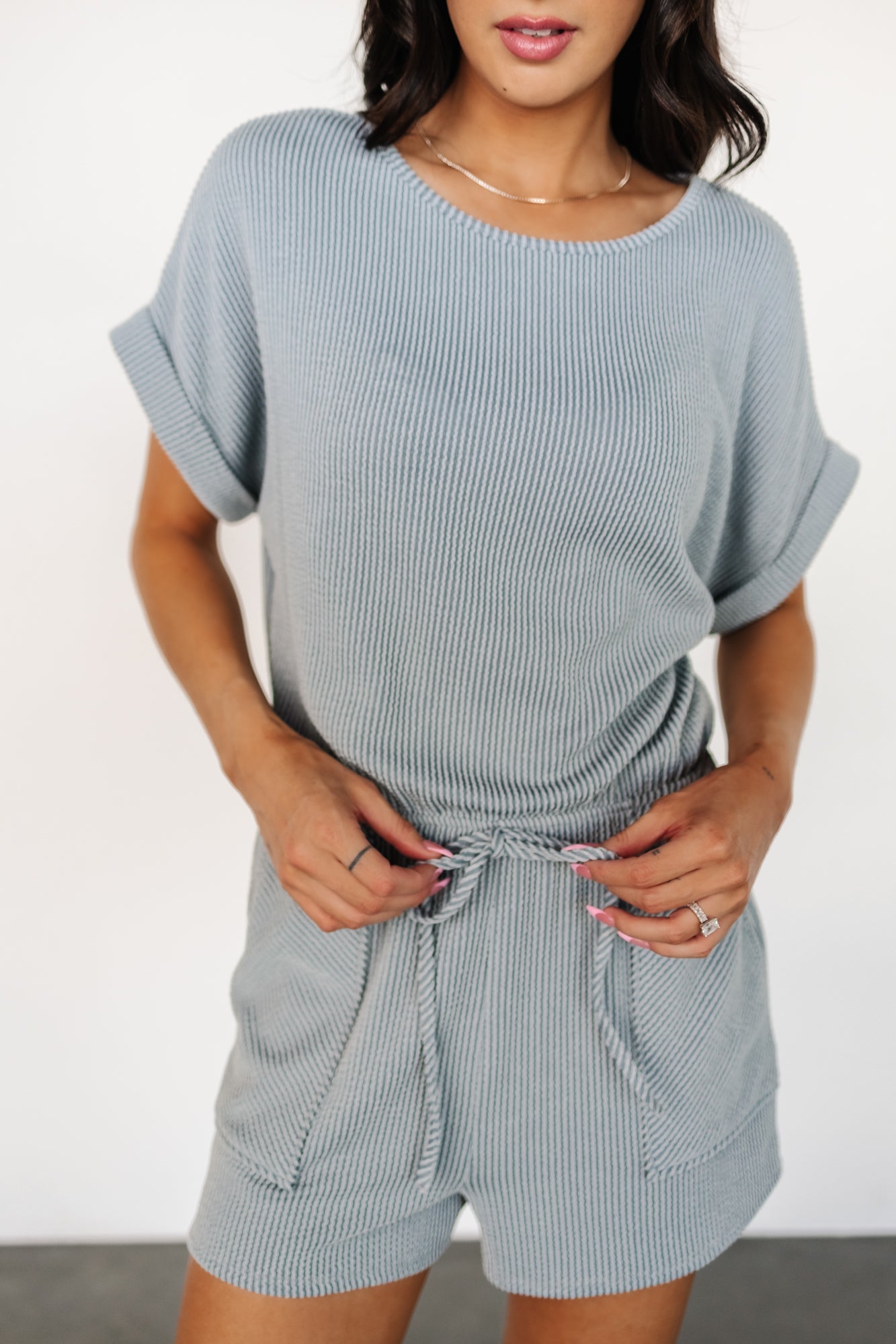 Side view of the Lely dusty blue romper highlighting raised fabric pattern, cuffed sleeve detail, and relaxed short length for easy movement.