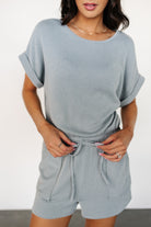 Side view of the Lely dusty blue romper highlighting raised fabric pattern, cuffed sleeve detail, and relaxed short length for easy movement.