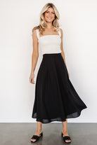 Full-length on-model image of the Katie pleated midi skirt in black highlighting the pleat structure, high-rise silhouette and hidden side pockets.