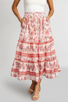 Model front view wearing Meg tiered midi skirt in blush multi floral print, showing smocked elastic waistband, soft tiers, and side pocket detail.